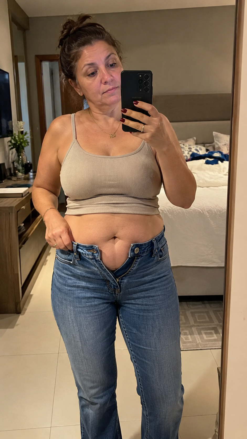 Carla antes: de calça jeans com o botão aberto, em frente ao espelho
