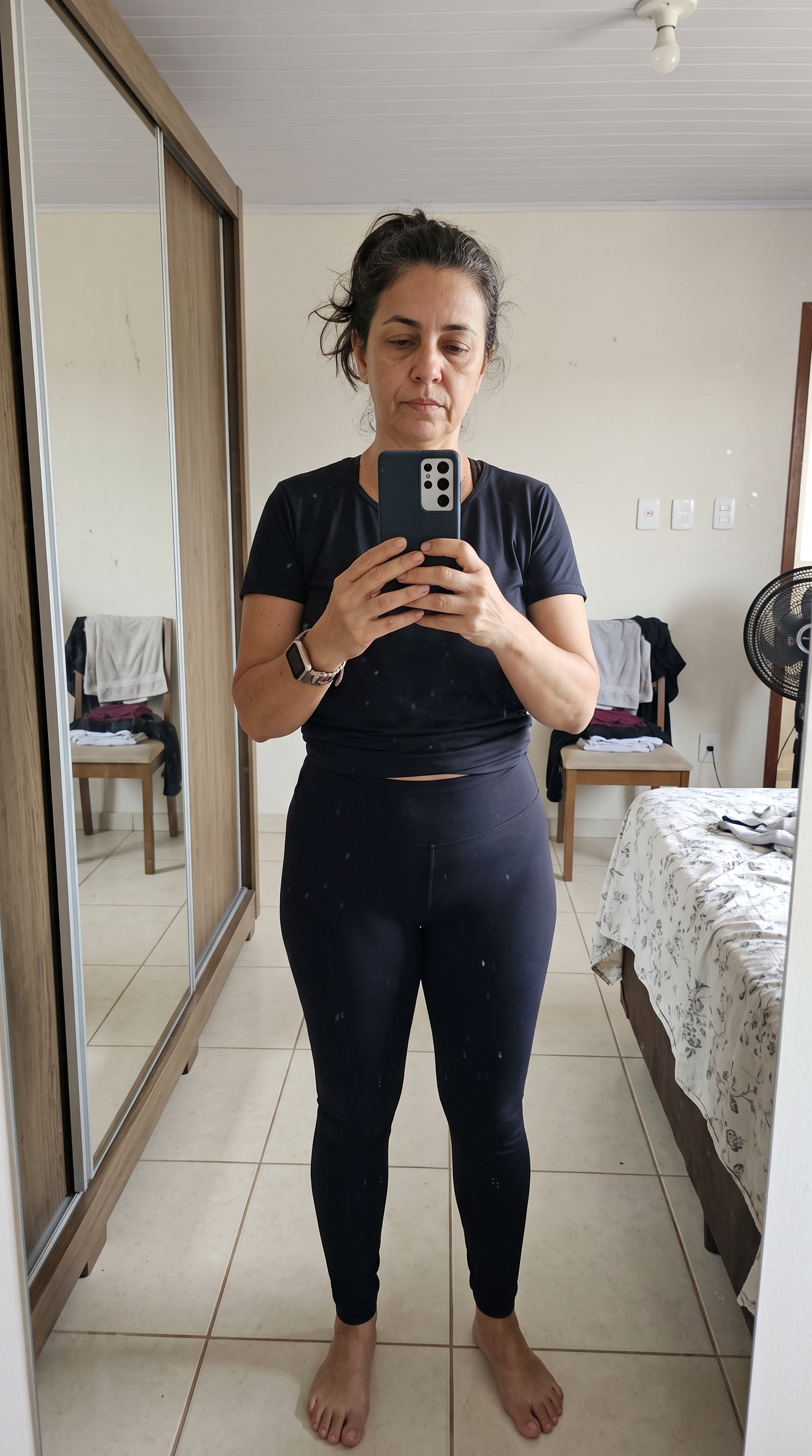 Lúcia antes: de roupa esportiva escura, fotografando-se no espelho do quarto